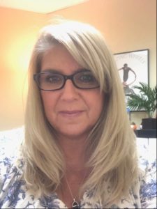 woman with long blond hair, slight smile and wearing glasses